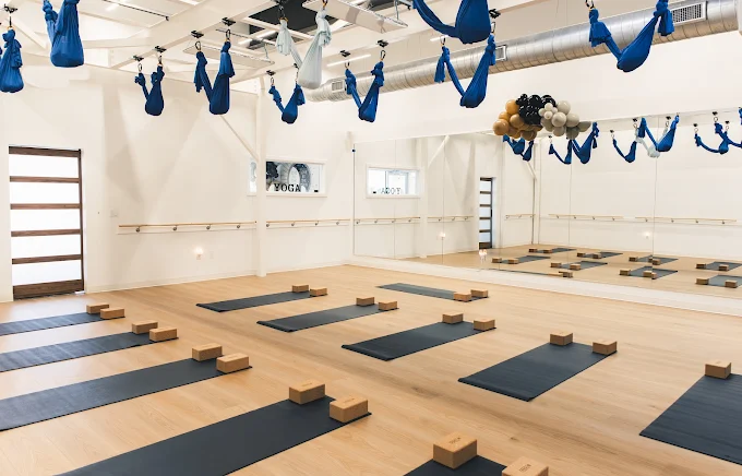 Moonshine Yoga Liberty Hill Studio Bright yoga studio at Moonshine Yoga Liberty Hill with mats, wooden blocks, mirrors, barre, and blue and white aerial yoga hammocks.